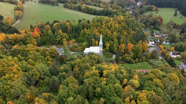 Aerial valley village church Travna Czechia autumn circle fast. The Czech Republic or Czechia historically known as Bohemia. Central Europe. Autumn fall season, brilliant colorful leaves along roads.