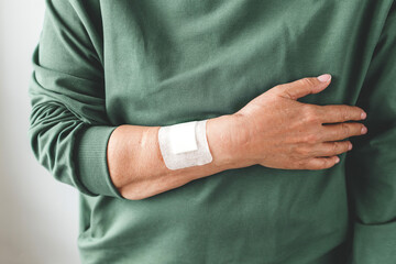 Close up of person with adhesive bandage on arm wearing green sweatshirt, symbolizing healthcare, recovery, vaccination, medical treatment and personal well-being