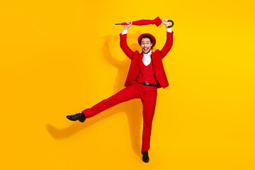 Energetic man in red suit leaps with umbrella against bright yellow background in playful showman vibe
