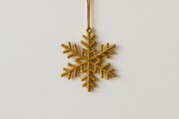 A single gold glitter snowflake ornament hangs suspended against a plain light background with plenty of copy space.