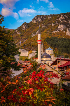 Scenic view of Travnik, Bosnia and Herzegovina, with a mosque minaret, colorful autumn foliage, and the old fortress under a mountain bathed in warm sunset light.