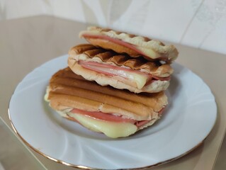 Stack of Three Pressed and Toasted Sandwiches (likely Tost or Panini) with Melted Cheese and Slices of Pink Ham, Served on a White Plate with a Gold Rim.