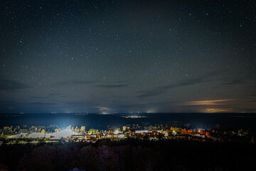 Fototapeta premium A clear night sky filled with countless stars above a distant landscape with faint city lights and clouds illuminated by a warm horizon glow.