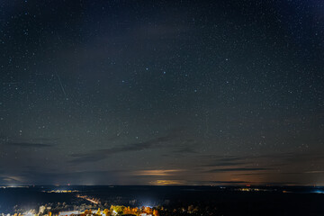 A clear night sky filled with countless stars above a distant landscape with faint city lights and clouds illuminated by a warm horizon glow.