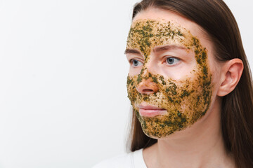 Portrait of young girl or woman with green natural homemade cosmetic mask on her face with white background. Concept of self-care at home or in salon. Copy space