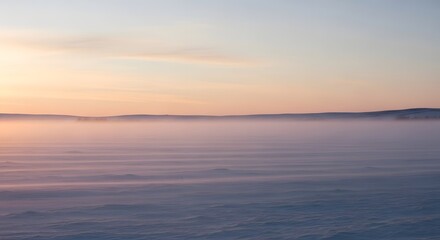 Obraz premium Sunrise over a snowy field with a layer of fog creating a dreamy scene