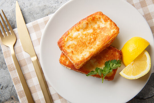 Saganaki is a Greek delicacy of fried cheese with a lemon wedge close-up in a plate on the table. Horizontal top view from above