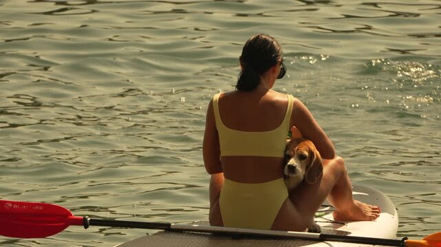 Woman, dog, paddleboarding, relaxing on a paddleboard in calm water on a peaceful summer day