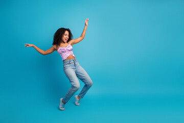 Obraz premium Young girl dancer in pink top and jeans jumps against blue background expressing joy energy and carefree lifestyle
