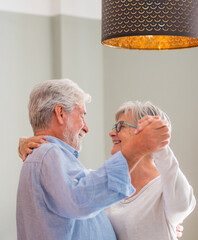 Joyful active old retired romantic couple dancing laughing in living room, happy middle aged wife...