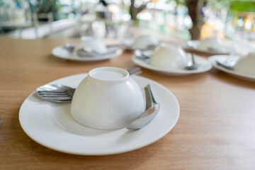 Multiple white bowls are placed upside down on plates with spoons on a wooden table in a restaurant.