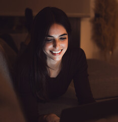 Fototapeta premium Close up of one young happy cheerful woman smiling and using laptop computer at home lying down on sofa working and studying alone at late night. Millennial girl surfing the net indoor with light