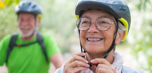 Portrait of one old woman smiling and enjoying nature outdoors riding bike with her husband laughing. Headshot of mature female with glasses feeling healthy. Senior putting on helmet to go trip  © Daniel