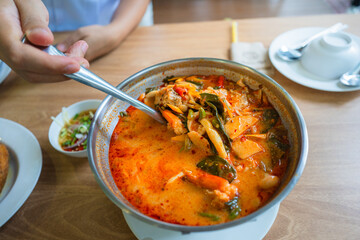 Woman serving steaming hot Asian soup into a bowl at a restaurant during a family meal - Young female diner at a table holding spoon full of Thai Tom Yum spicy soup with summer filter, from above
