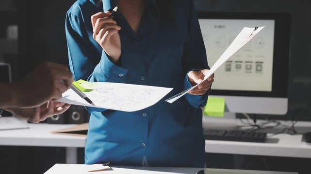 Group of young Asian uxui designers working together pointing at computer screen analyzing mobile app interface wireframes while working in a modern office