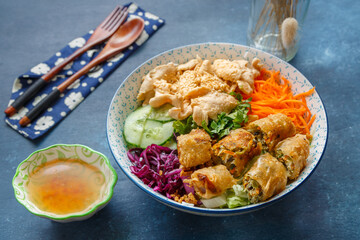 Bo Bun au poulet – salade vietnamienne de vermicelles de riz avec nems, lamelles de poulet et crudités, servie avec sauce sur fond bleu. Gastronomie vietnamienne.