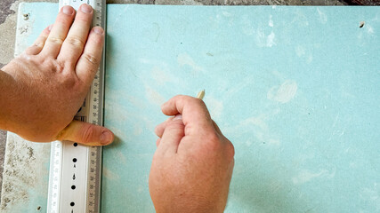 Rough hands of Caucasian male artist meticulously crafting woodwork mark on greenish panel,...