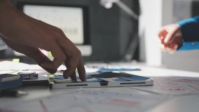 Group of young Asian uxui designers working together pointing at computer screen analyzing mobile app interface wireframes while working in a modern office