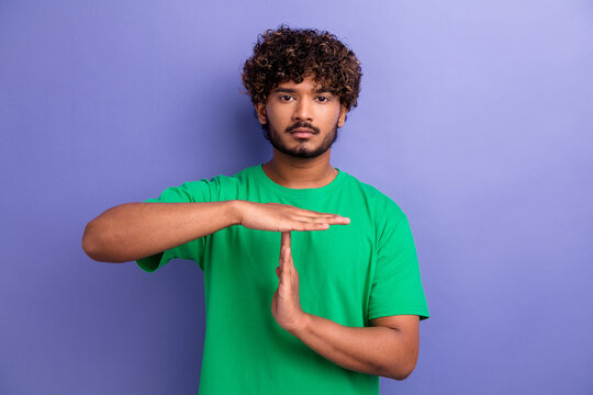 Positive casual male making a timeout gesture against a simple vibrant purple background showcasing green fashion.
