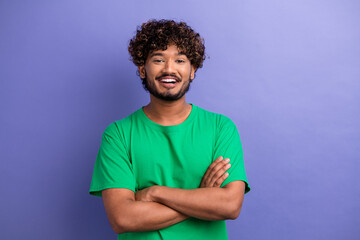 Happy young man in green t-shirt standing with arms crossed against purple background, showcasing confidence and positivity