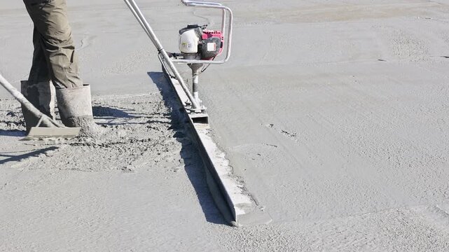 Contractor use screed to level freshly poured concrete on construction site in broad works day
