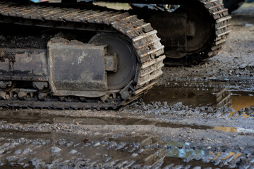 Steel crawler tracks of heavy construction excavator standing on wet muddy terrain, representing durability, traction, and reliability of tracked machinery used for ground and earthmoving operations