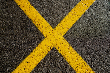 Bright yellow X sign painted on dark asphalt, representing warning or restriction zone, urban...