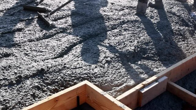 Construction workers pour wet cement from chute into wooden formwork building site cement is being poured over rebar grid that provides structural reinforcement for concrete foundation