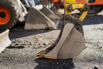 Excavator digging bucket positioned on asphalt surface showing wear marks, hydraulic connection, and metal precision construction equipment used in earthmoving, roadwork, and industrial projects