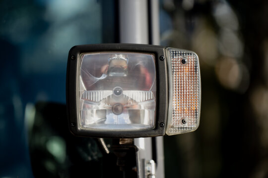 Square headlight and side indicator lamp on construction vehicle showing durable industrial design, clear glass housing, and mechanical precision used for worksite safety and equipment reliability