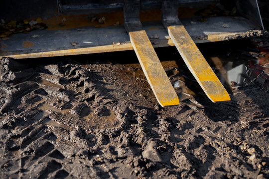 Forklift or loader fork attachment resting on muddy construction site ground showing metal tines, dirt texture, and mechanical strength, representing industrial material handling and outdoor equipment
