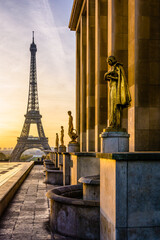 Sunrise on the Eiffel Tower and the golden statues of the Trocadero esplanade along the Chaillot palace in Paris, France.
