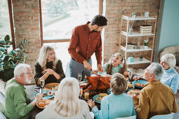 Fun and warm family gathering around the table as a cheerful host carves a turkey for grandparents parents and children during a joyful feast