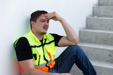 Construction worker in safety vest sitting on stairway with hands on head, showing signs of stress, fatigue, or headache. Concept of burnout, job pressure, mental health, and labor exhaustion.