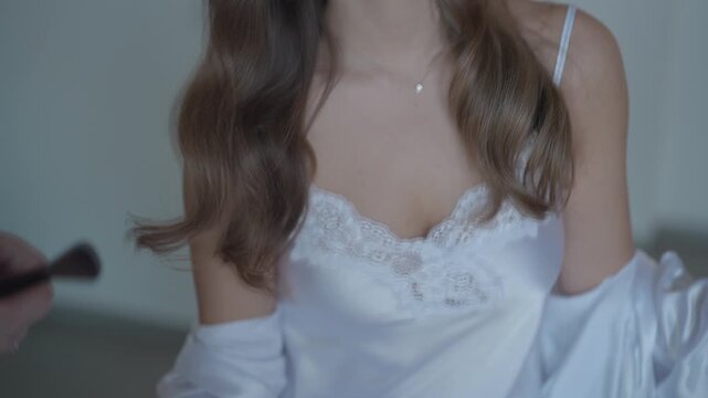 A close-up' slow motion video captures a beautiful young woman in a white silk or lace top as she delicately touches and adjusts her long, wavy hair. Ideal for themes of beauty, fashion and self-care.
