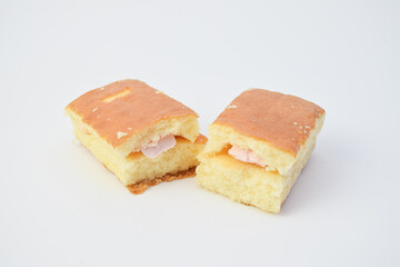 Close-up of sponge cake cut in half with pink cream filling, minimal food photo on white background, soft texture dessert for bakery, snack, or sweet breakfast concept.