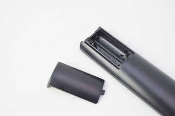 Close-up of black remote control with open battery cover on white background, minimal electronic object composition suitable for technology, repair, or device concept.
