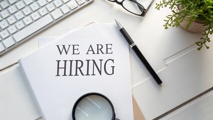 Flat Lay of We Are Hiring Text Under Magnifying Glass on White Desk for Recruitment Concept