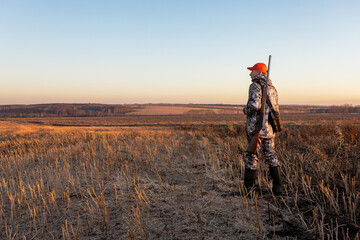 Mature man hunter walks field at sunset or sunrise. Hunting, leisure activity, hobby in fall season.