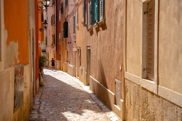 Rovinj, Croatia - August 15, 2025: A jogger runs along a sunlit cobblestone alley lined with pastel walls and shuttered windows, capturing the calm of an early morning.