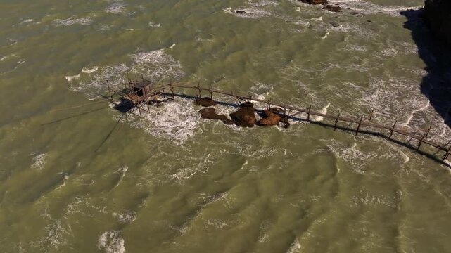 Drone view of the iconic trabocco at Punta Aderci with clear blue sea, visible sandy seabed, and gentle Adriatic waves on a sunny October afternoon.