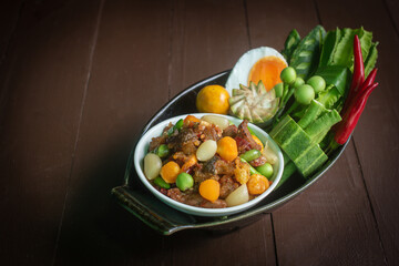  still life of authentic Nam Prik Long Ruea, a traditional Thai chili paste dip, presented in ceramic bowls on a wooden board and banana leaf. The composition includes fresh seasonal vegetabl