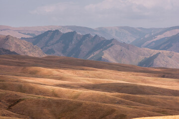 Dry steppe and gently rolling hills against a hazy mountain range. A natural landscape on a sunny autumn day.