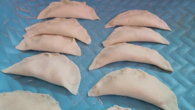 Karanji (Gujiya) are uncooked, crescent-shaped pastries arranged in rows. They are a traditional sweet prepared for Indian festivals like Diwali, filled and sealed before being fried.