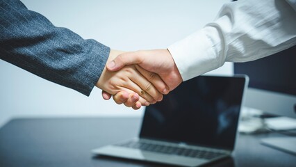 Obraz premium Two business people shaking hands over a laptop isolated on white background isolated on transparent background