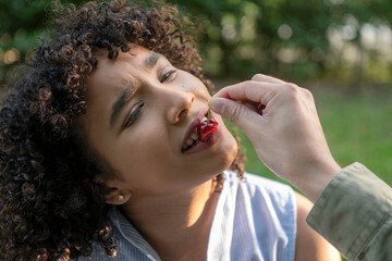 Man feeding cherry to woman at park picnic