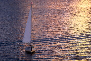 Sailing into the Sunset: A lone sailboat glides effortlessly across the shimmering water under a sky painted with the golden hues of the setting sun, evoking a sense of serene freedom and adventure.