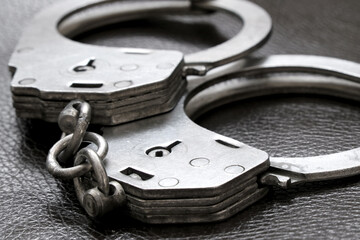 This is a closeup view of metal handcuffs resting on an elegant black leather surface
