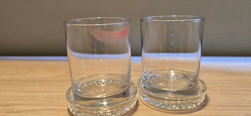 Two glasses of water and coasters are placed on a wooden table. After use, one has women's lipstick marks on the rim. The glass is empty and there is no drink. Drink all the pure water in water cup. 

