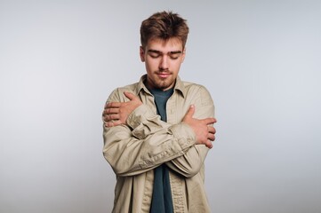 Young man expressing self-embrace and contemplation in a studio setting during daylight hours